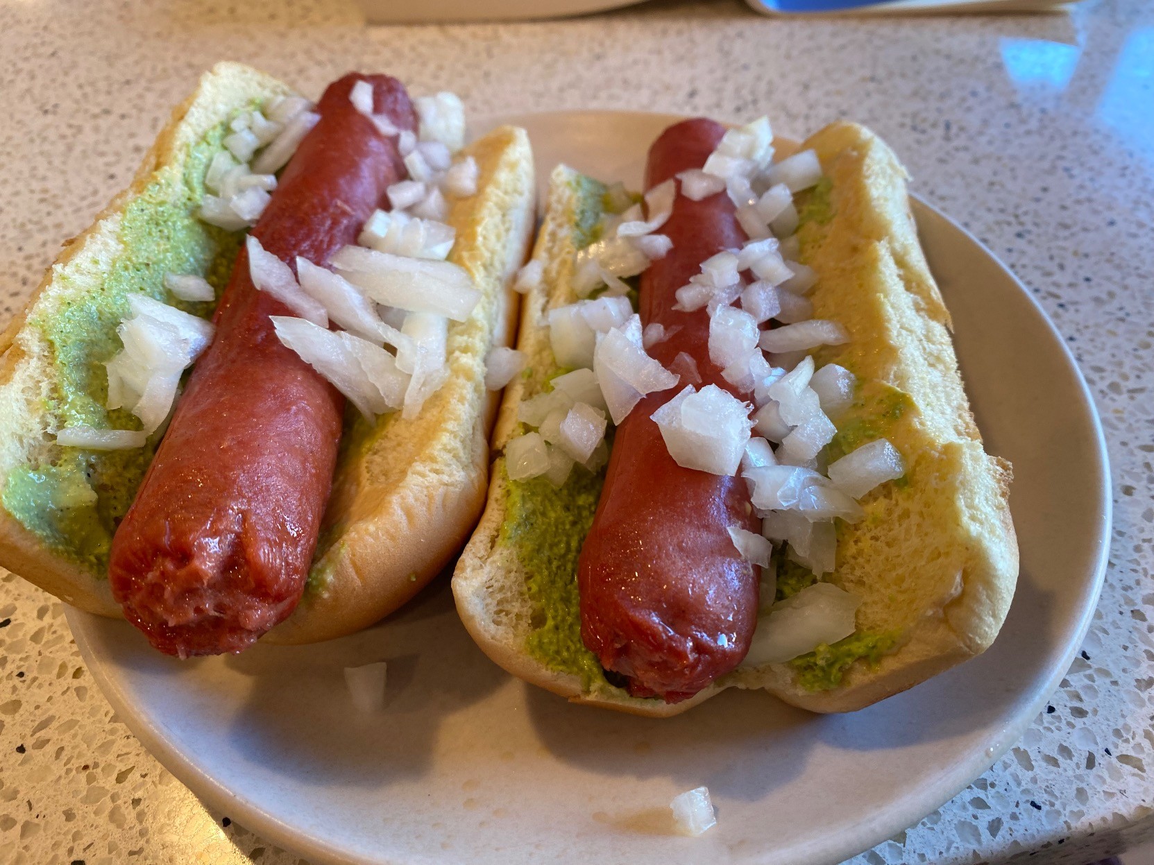 ECU two hotdogs side by side on a small white plate, vertical-orientation low-angle perspective, on buns. each have jalapeño-cilatro-mayo on one shoulder, dijon on the other, chopped onions on both