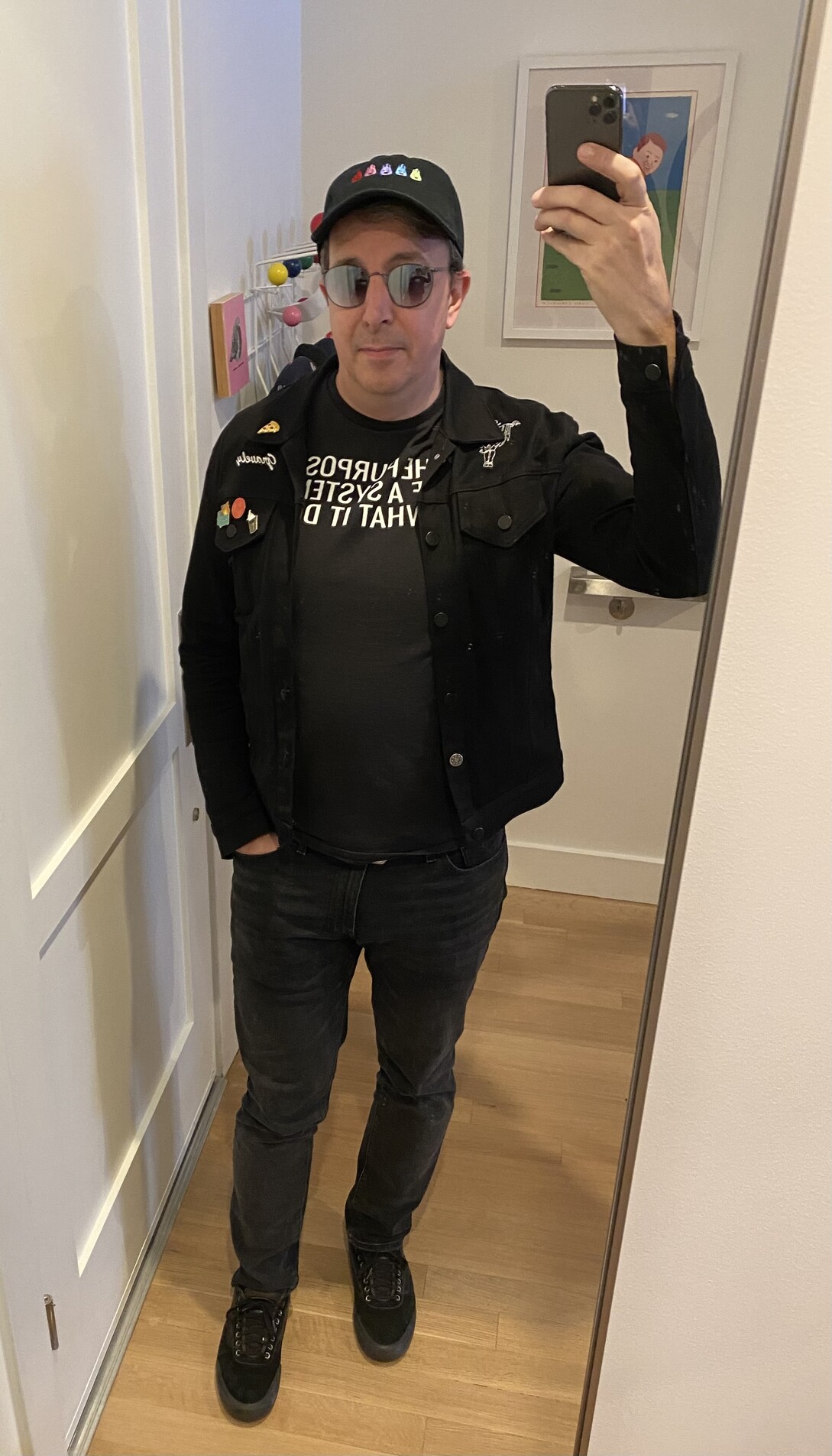 full length selfie of me, black baseball cap, black "gravely" embroidered jean jacket, black "the purpose of a system is what it does" t-shirt, black jeans, back tennis shoes, mirror shades