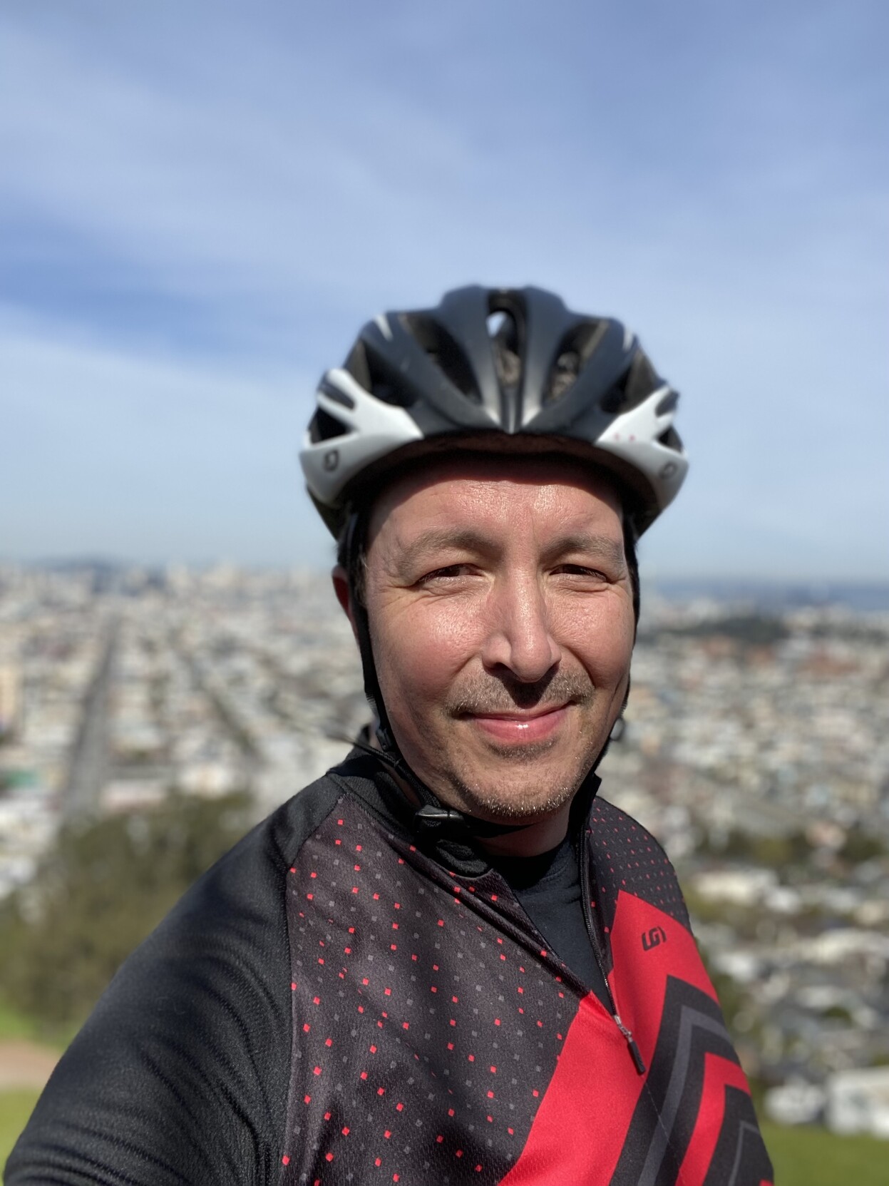 selfie in a black and red polka dot cycling shirt from the top of bernal heights park, downtown sf behind me. i wore a cycling shirt because i wanted all the rear pockets for my keys and snacks and stuff like that