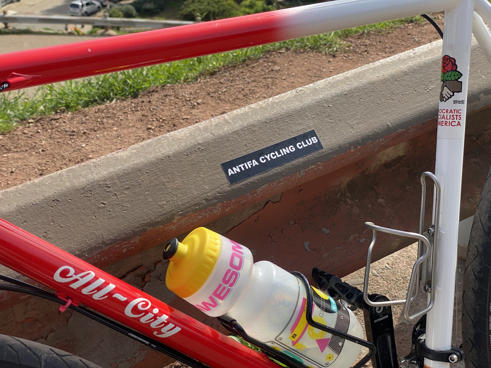 the front triangle of my bike leaning against a guard rail, the guard rail has a sticker on it that says ANTIFA CYCLING CLUB