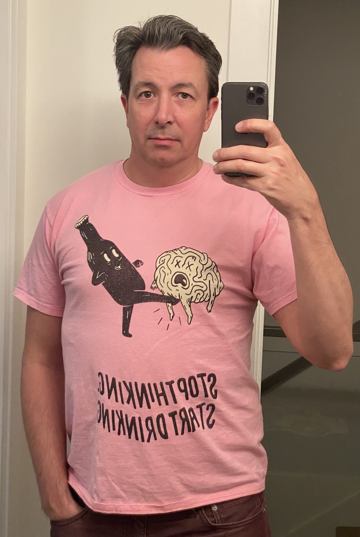 selfie, receding hair line pompadour?? 40-something in a pink t shirt that fits, with a woodcut style illustration of a bottle kicking a brain between its legs over the slogan "stop thinking / start drinking" on it