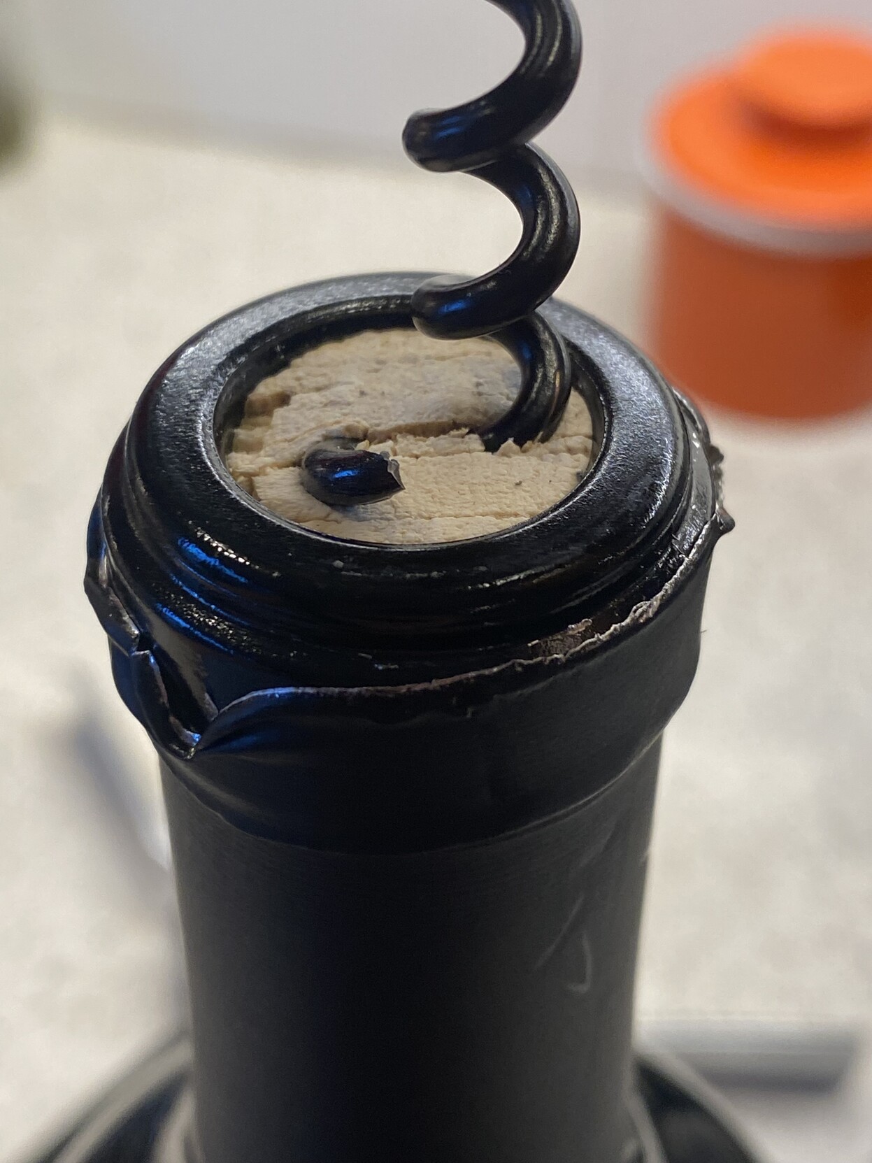 ecu corked bottle of red wine with a bit of corkscrew protruding from the top left off the corn and a full corkscrew entering it from the top right