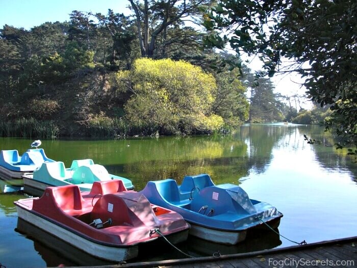 Photograph of Stow Lake with four fiberglass 2x2 boards on a small lack moored at a wooden dock, trees surround(photo from duckduckgo images search, but we were in a red one like that)