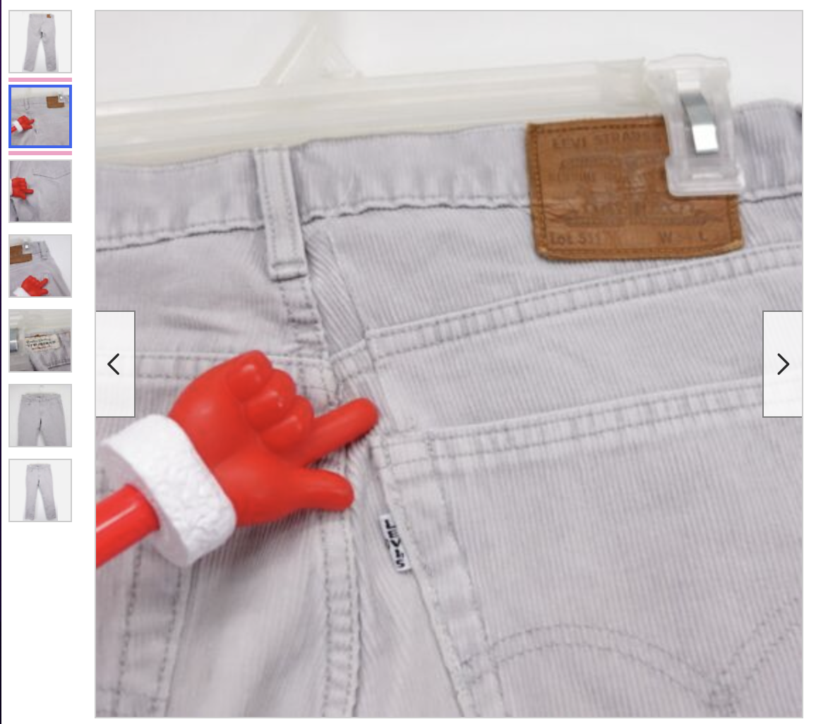 ECU photograph from an ebay listing of the back right pocket and waist and leather label-belt-loop of a pair of gray levis corduroy pants the photographer has used what looks like a tiny baby-sized red gloved hand (made of plastic) on a red stick with a white styrofoam cuff (?) to indicate where the pants were repaired