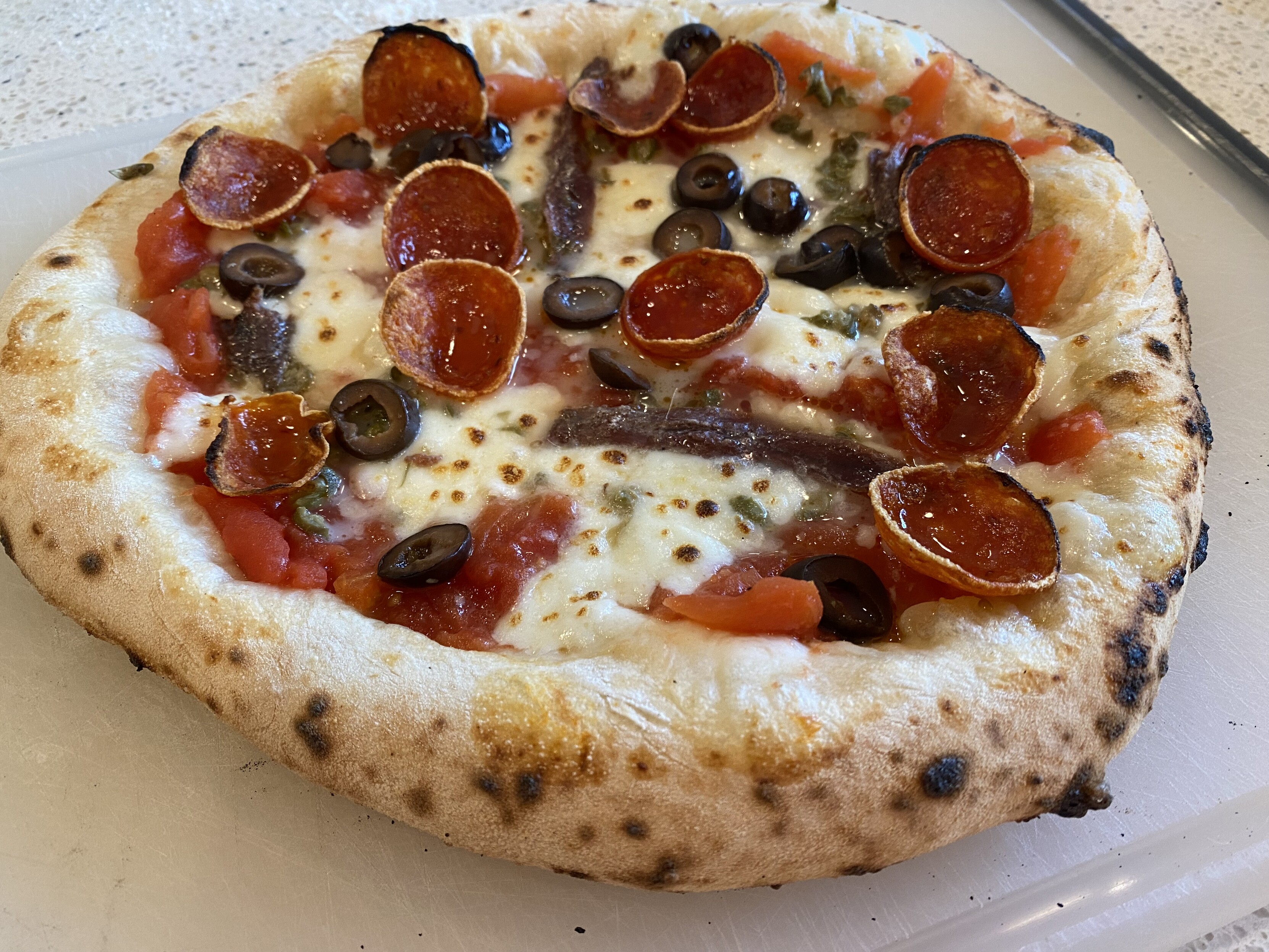 neapolitan pizza baked ?0 seconds at 950F, on the board to be cut, topped with hand crushed san marzano, anchovies, capers, black olives, mozz, pecorino, pep, olive oil