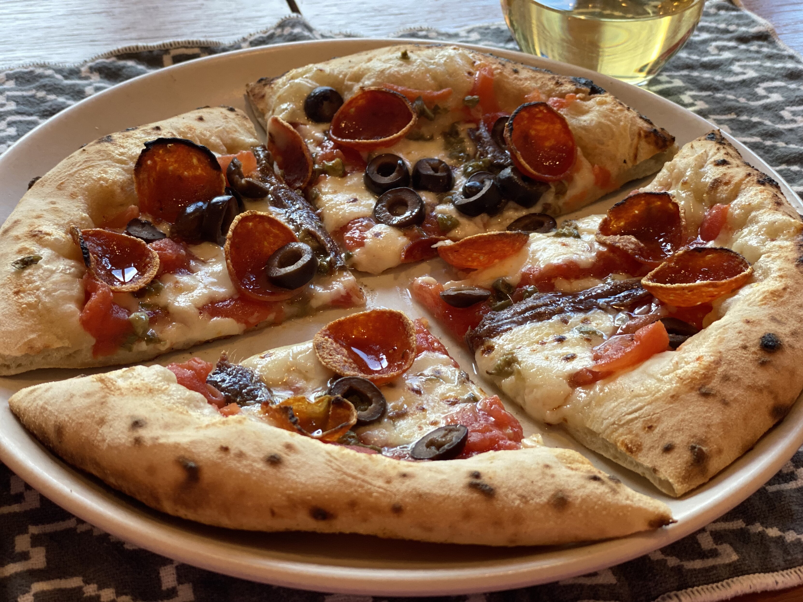 neapolitan pizza cut and served, topped with hand crushed san marzano, anchovies, capers, black olives, mozz, pecorino, pep, olive oil, with a glass of wine