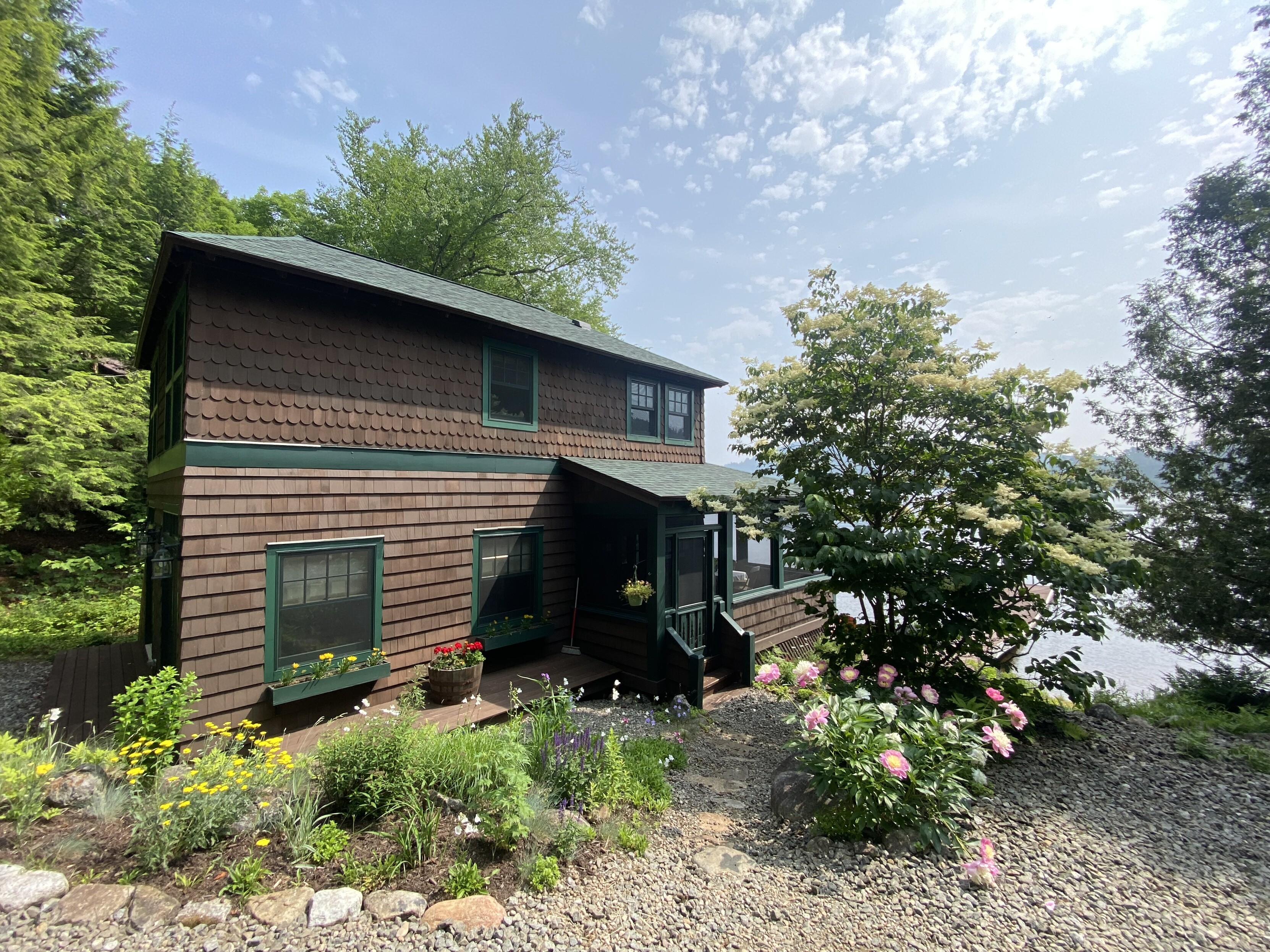 a lake house on upper saranac lake, side view, flower gardens surround the path to the porch, lane in the bottom right