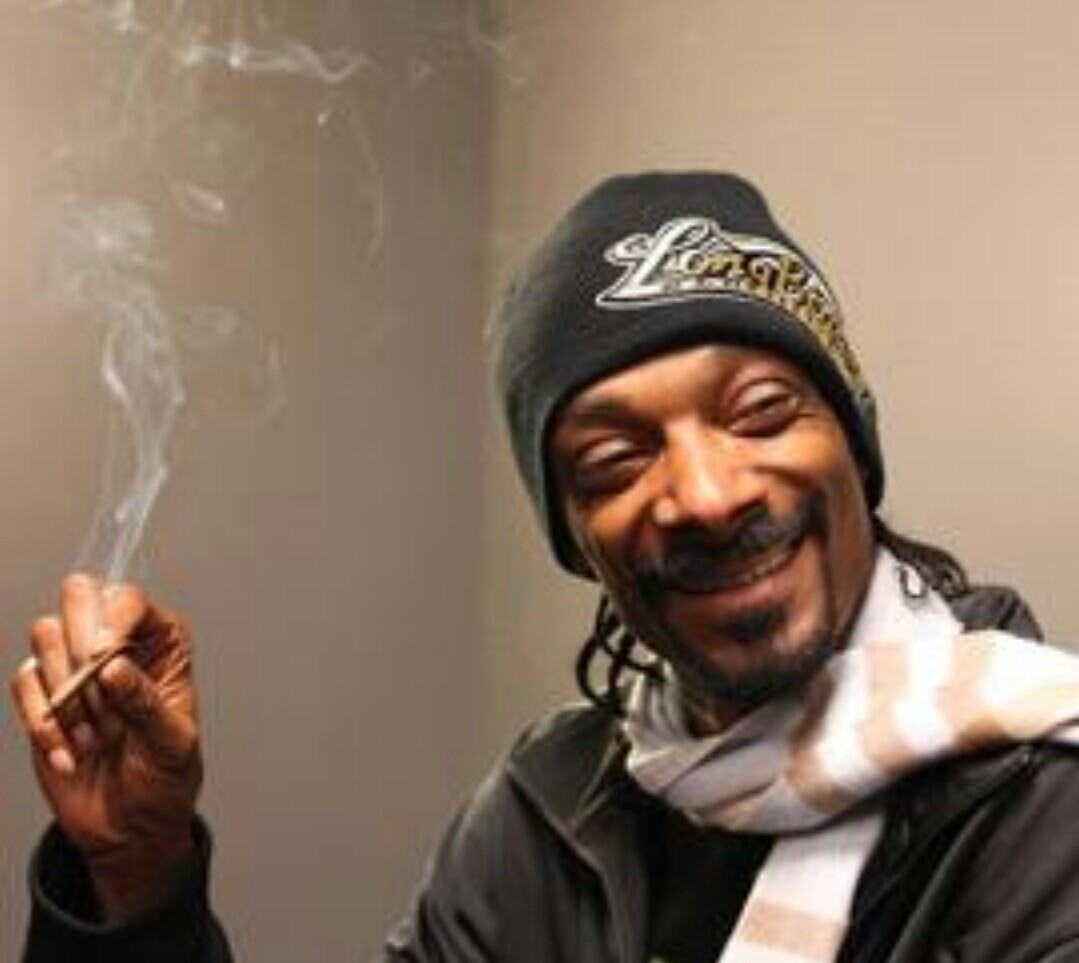 snoop dog holding a joint, laughing, looking right, wearing a gray winter cap and white and tan striped scarf