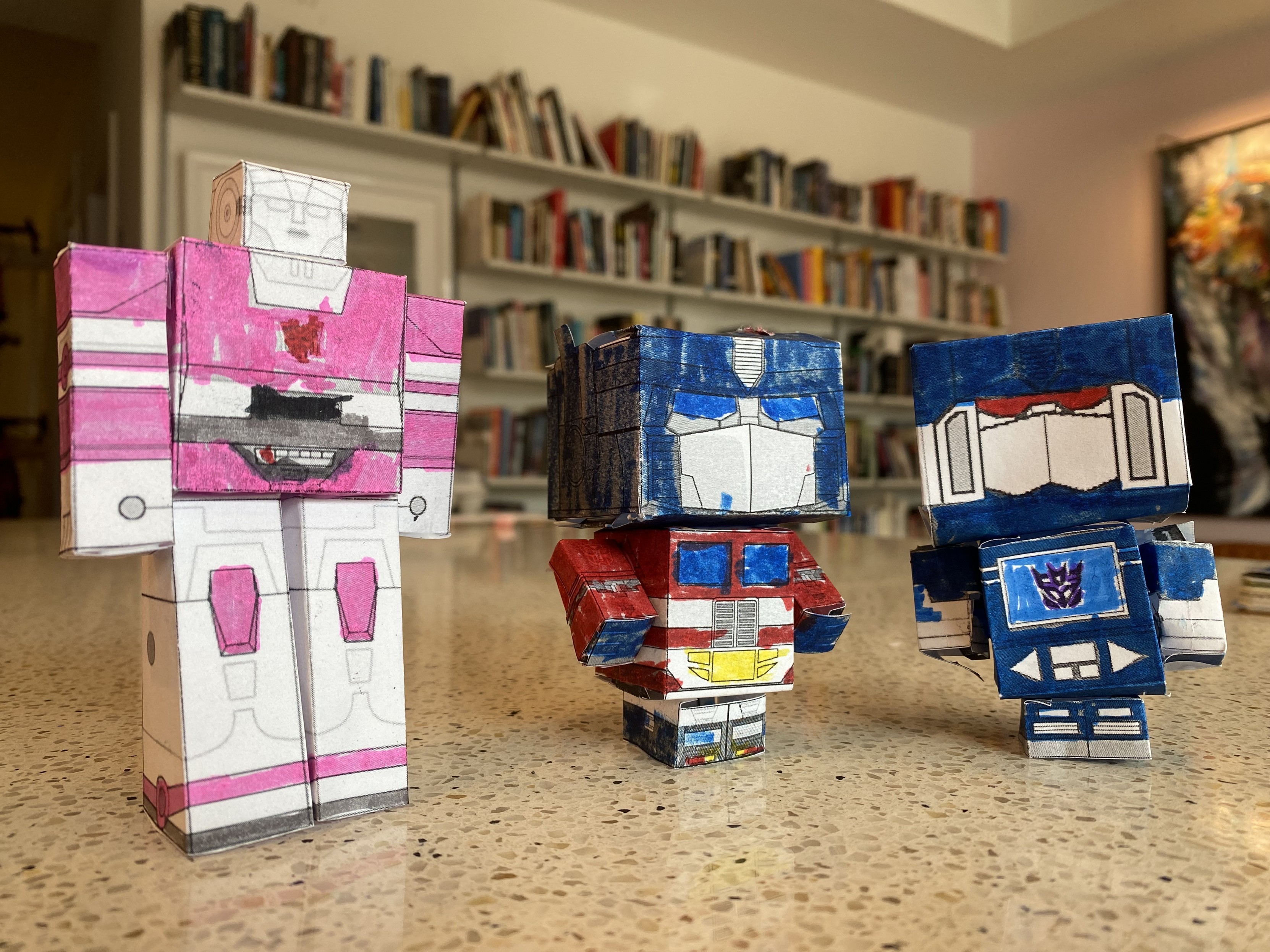 arcee, optimus prime, and soundwave transformers in robot mode, papercraft, colored by a 5y old, assembled poorly by mei made the first one correctly with slots and tabs, after that, fucking nope, used elmer's glue