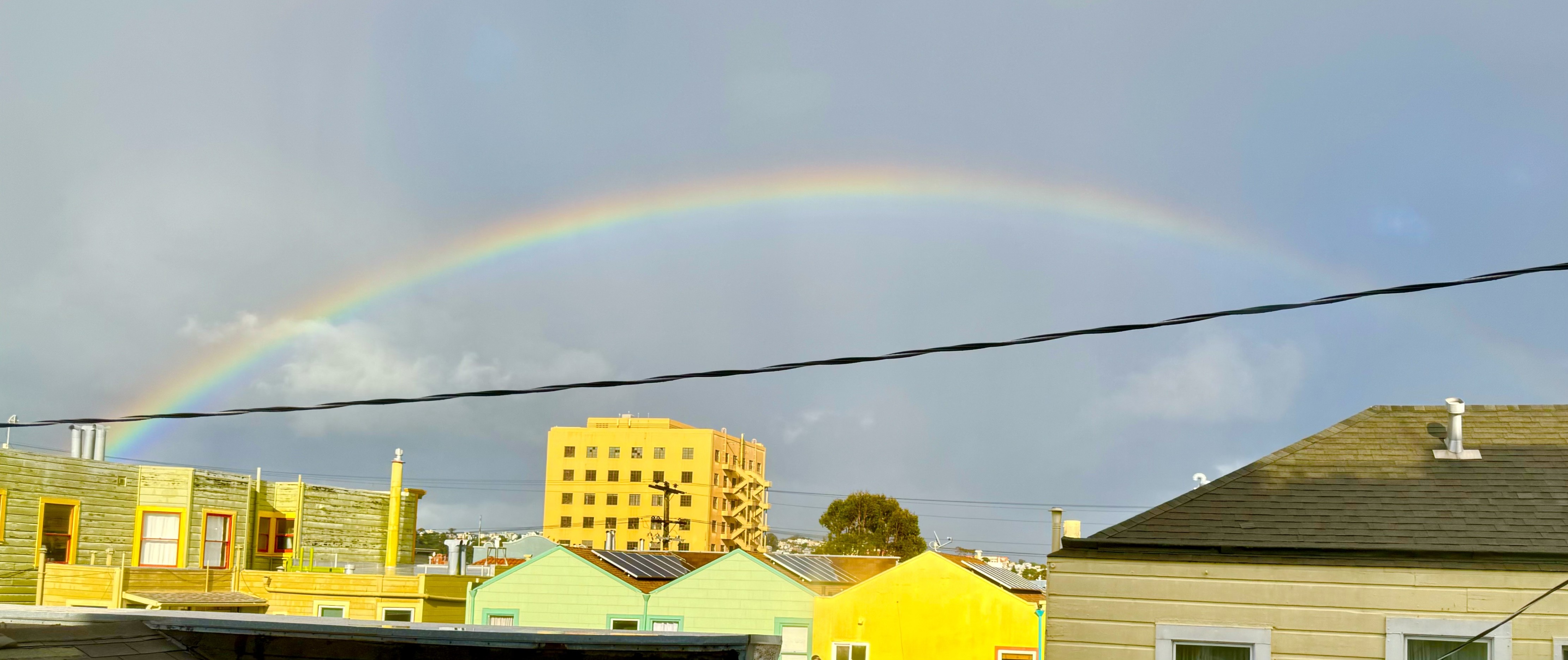 a cropped and oversaturated photograph out of a window of a rainbow over the mission in san francisco.