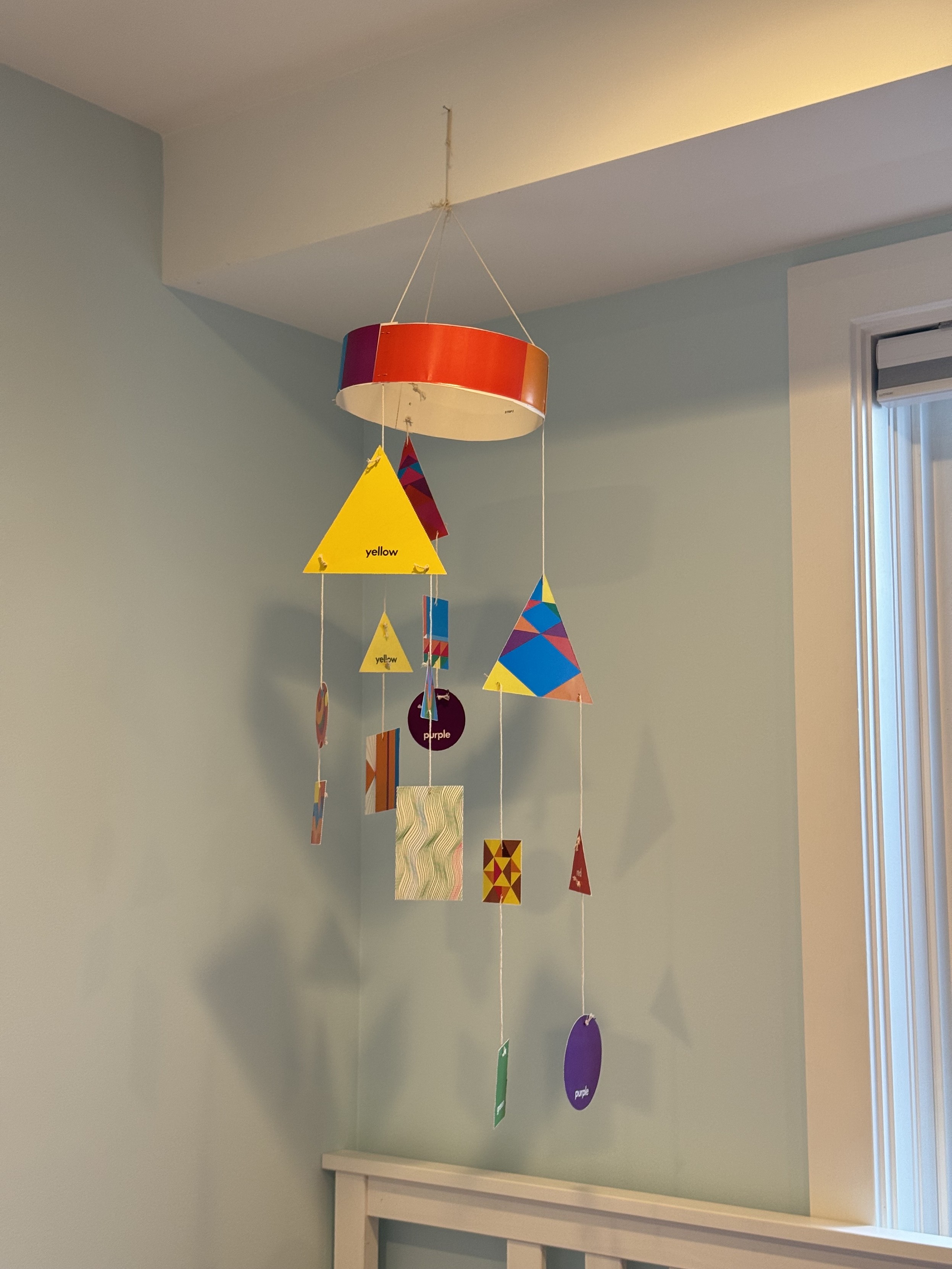 a photograph of the assembled mobile hanging over my kid’s bed. the wall behind the bed is a light blue, the ceiling and window trim are white