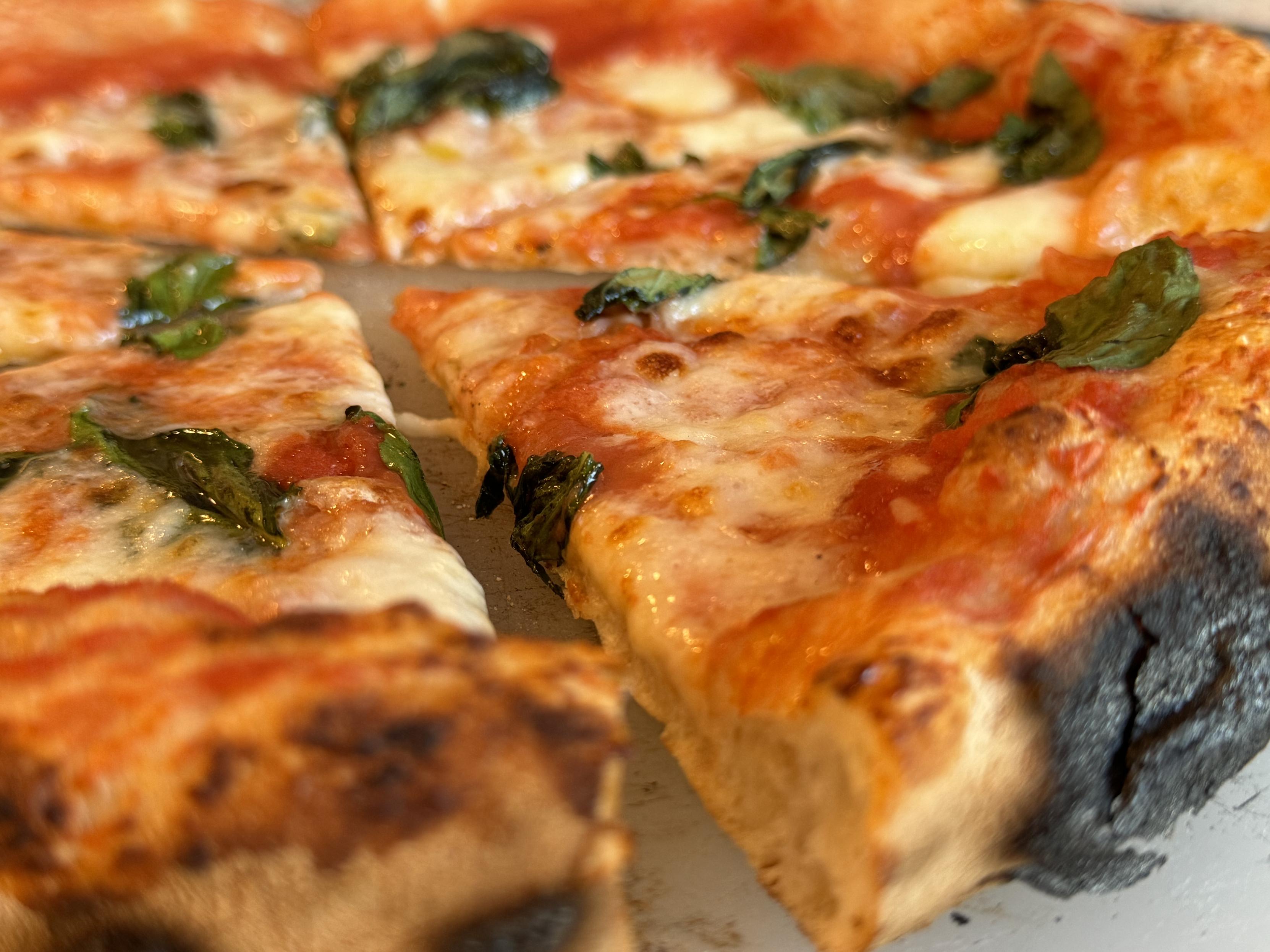 macro photo of a Neapolitan pizza w/ sauce, cheese, and basil, sliced, showing off the crust