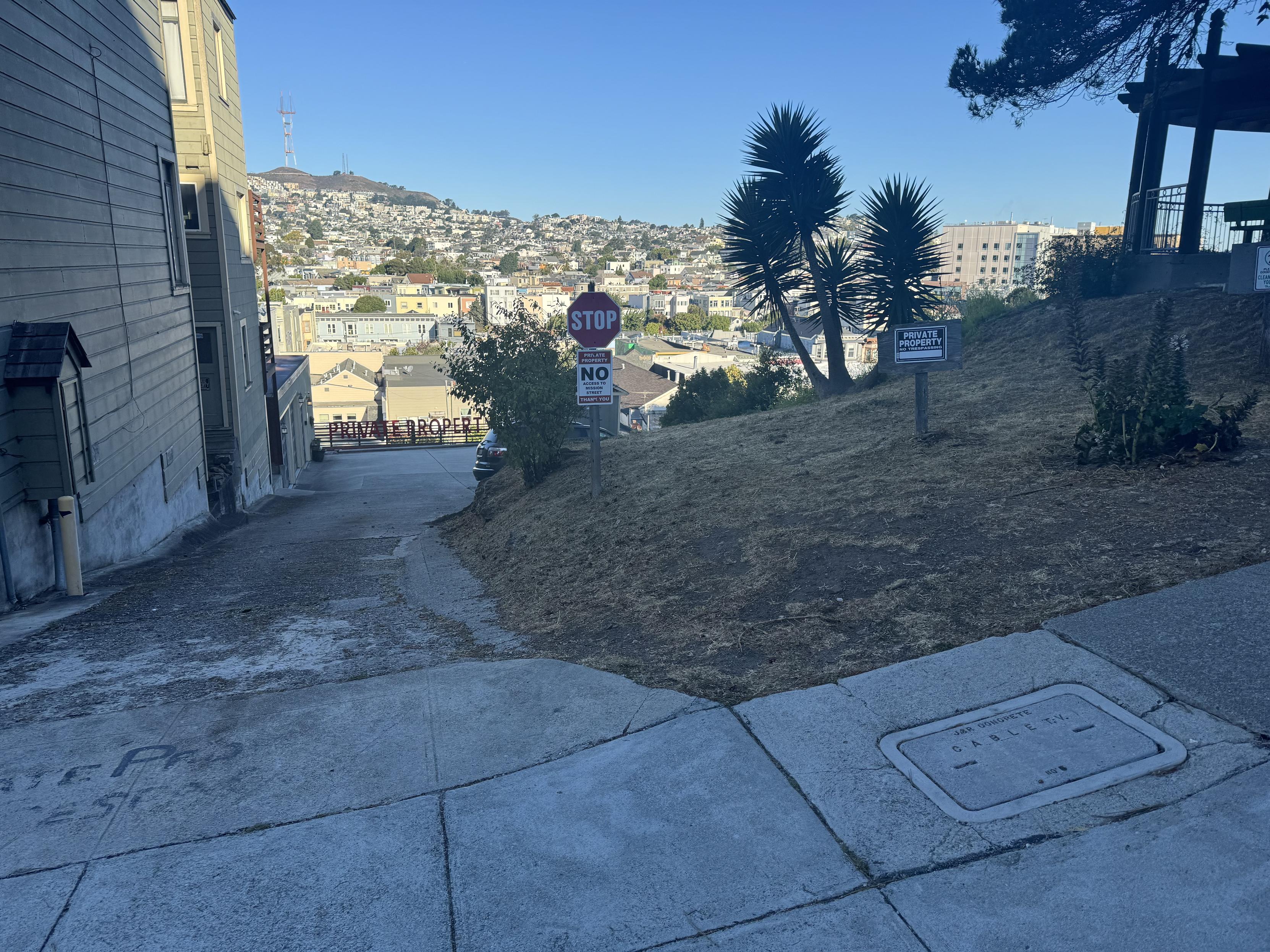 photograph of san francisco looking north-west from 100-ish Coleridge St downhill, down a driveway with a building to the left and a park to the right. IN the center is a store-bought STOP sign. Under the stop sign is a nice (I guess, if you have to have it) custom sign explaining that there is no way to get to Mission Street (the other side of this block) from here. To the right is a store-bought generic private property sign. At the bottom of the driveway, and this is the new thing, the residents have bought two foot high letters and spelled out PRIVATE PROPERTY along the fence at the bottom of their driveway. if you’ve been descending straight down the hill from Bernal, you’ve heretofore enjoyed:1. mid-block steps through a garden2. a half block of Emerelda Ave3. another set of mid-block steps through a garden4. another half block of Emerelda Ave5. another set of mid-block steps through a garden6. private property signs