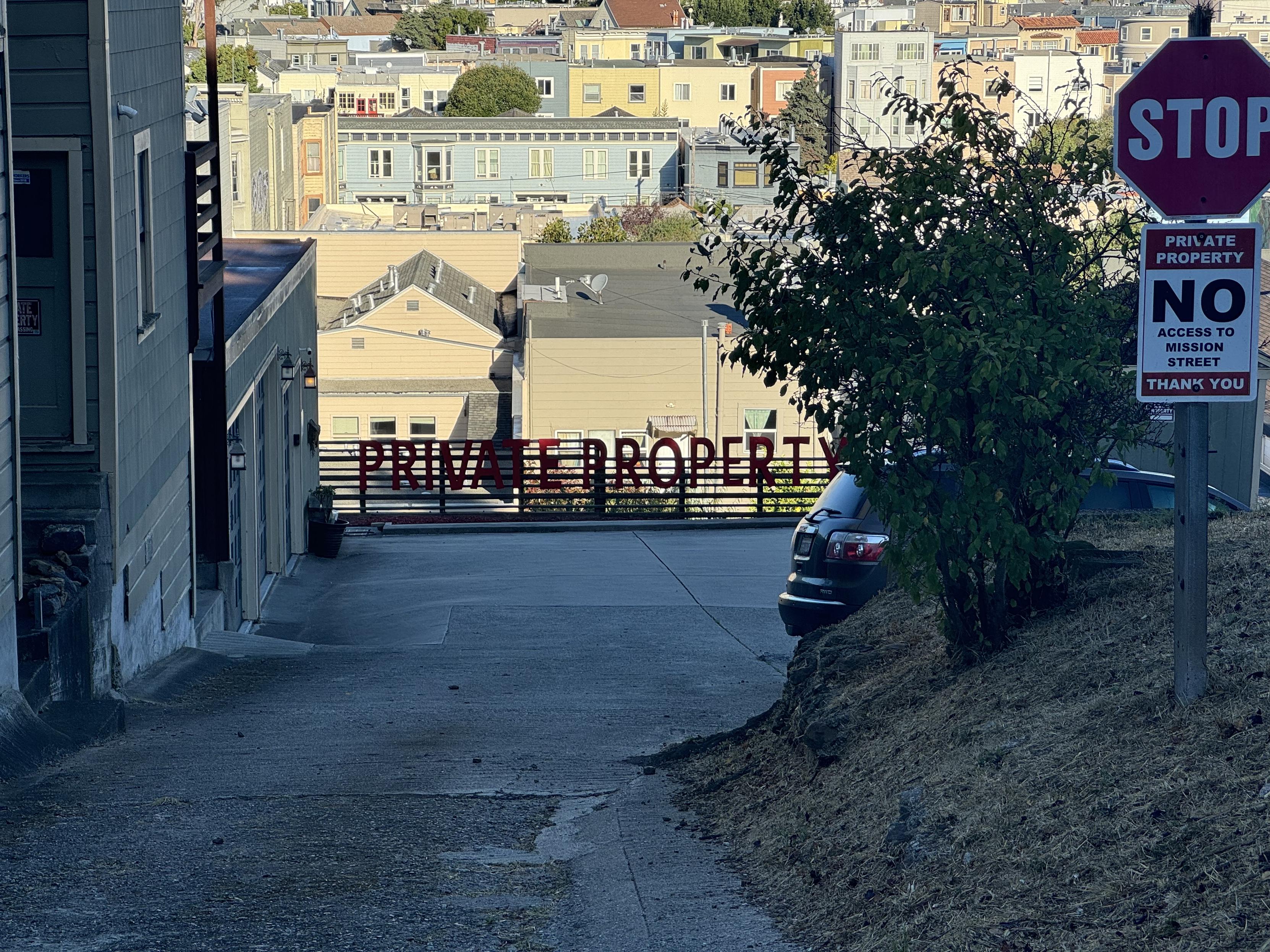 photograph of san francisco looking north-west from 100-ish Coleridge St downhill, from the same vantage point as the prior photo, but zoomed in on the two foot high letters and that spell out PRIVATE PROPERTY along the fence at the bottom of the driveway. it’d be cool if there was a zip line / gondola across to noe from somewhere along this dumb route.