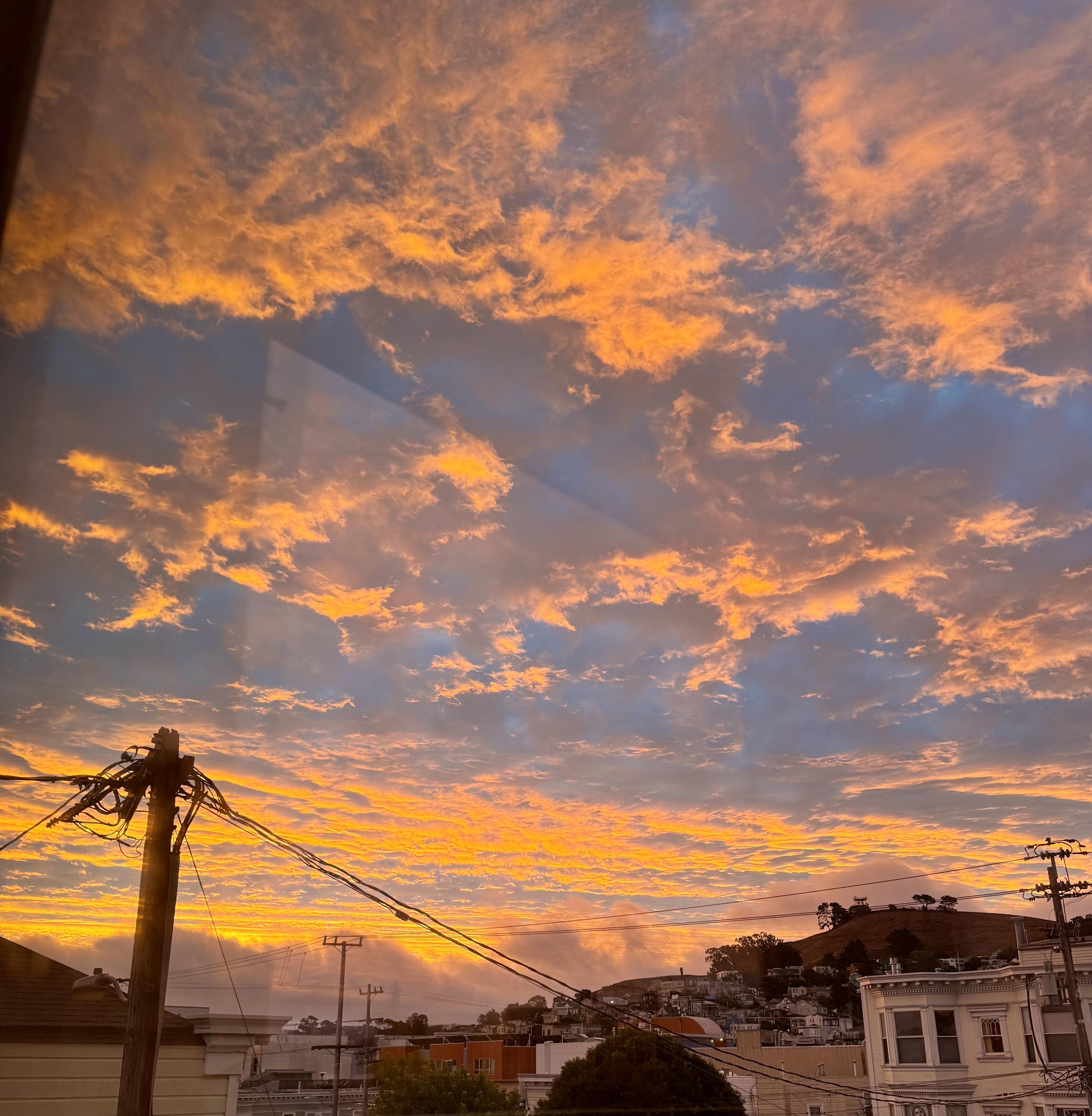 photograph of san francisco in the mission looking southeast at sunrise this morning (some dox) the sky is streaked with orange-lit clouds over a blue sky backing, but low at the horizon and heading east, a thick gray cloud bank roils slowly