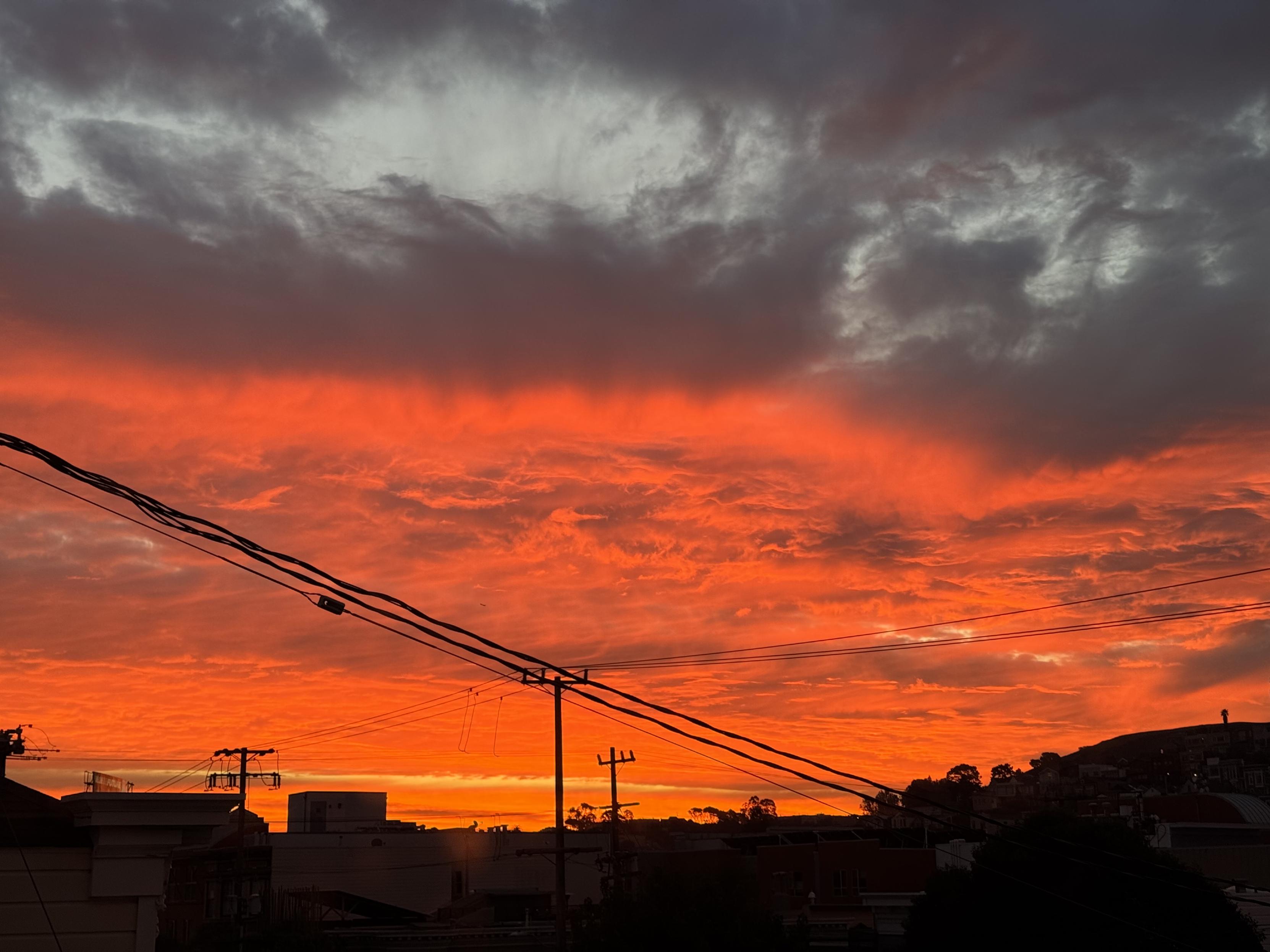 sunrise over the mission, the center, most distant bands of clouds are bright orange, the nearest high clouds are white and blue