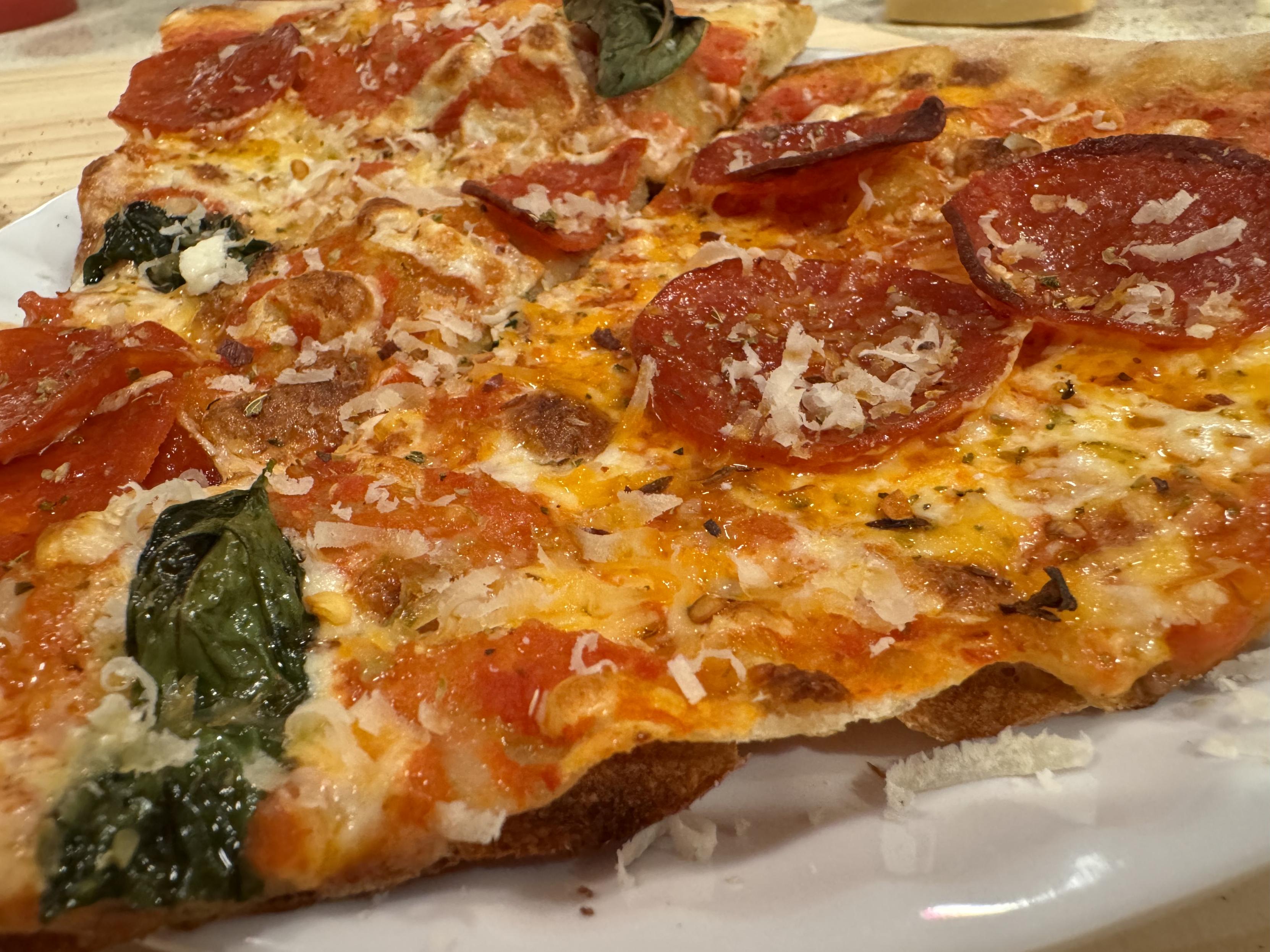 macro of one plated slice, finished w/ shaved parm, red pepper flakes, and oreganothe very thin crust is visibly bubbled and a burned bottom layer has pulled away from the rest of the crust in waves