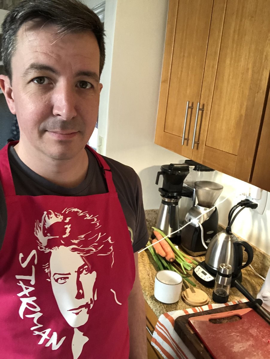 getting ready to prep dinner by donning a hot pink ‘David Boogey’ “STARMAN” apron