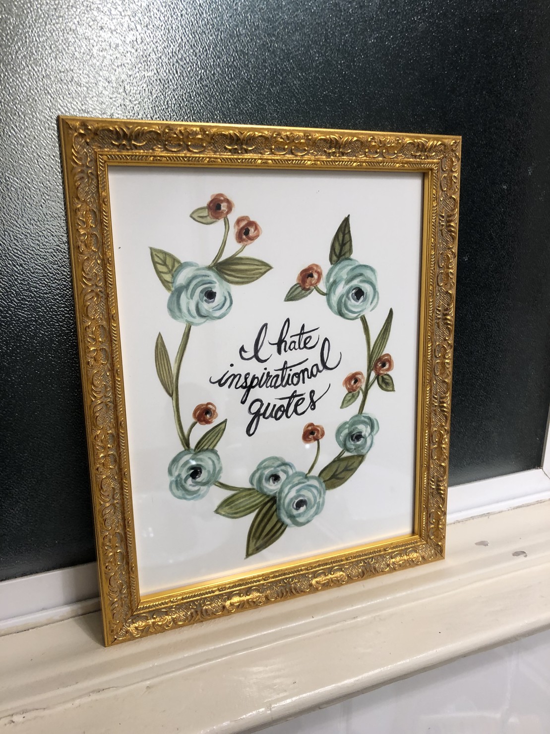 watercolor on bristol, flowers encircling “I hate inspirational quotes” in black script, ornate carved frame in gold