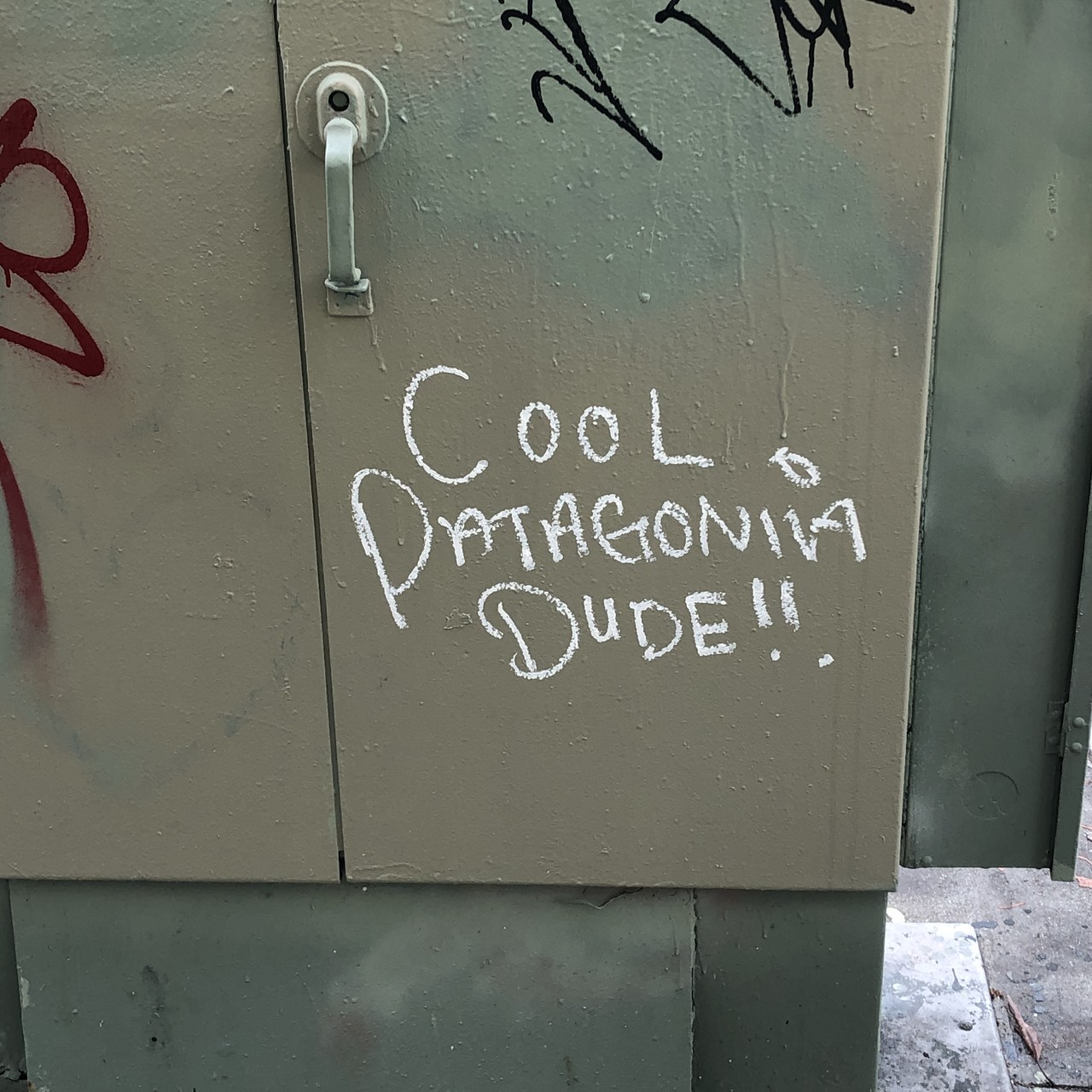 “COOL PATAGONIA DUDE!!” chalked on a telephone utility box